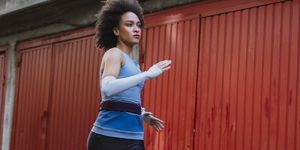 young female afro american athlete running outdoors next to a row of garages