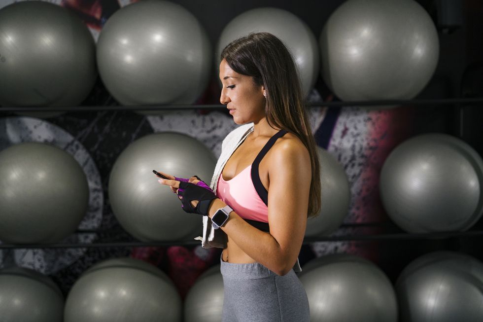 young female athlete using mobile phone by fitness balls at gym