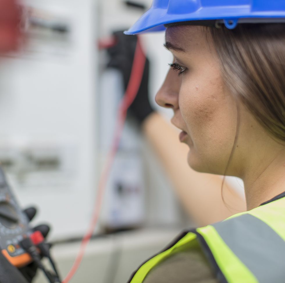 young female electrician working with voltmeter at fusebox