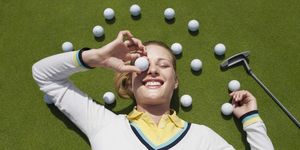 young female golfer lying on green, holding ball in front of eye, view from above