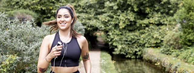 young female runner listening to earphones while running on riverside path