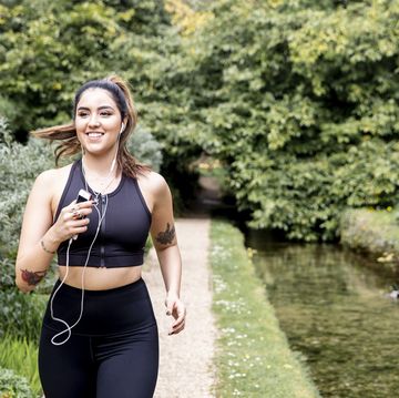 young female runner listening to earphones while running on riverside path