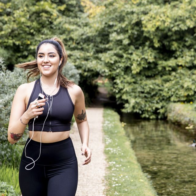 young female runner listening to earphones while running on riverside path
