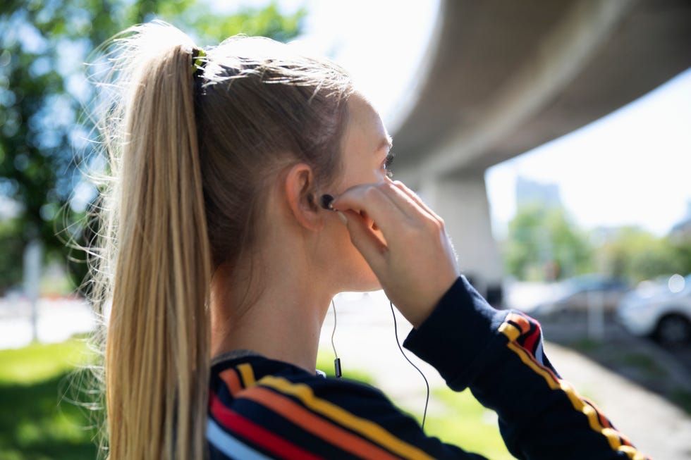 Young female runner putting earbud headphones in ear