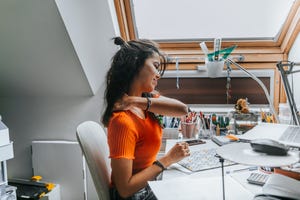 young female student with neck pain while sitting on desk preparing examns