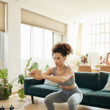 young fit woman doing squats in living room