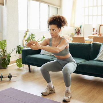 young fit woman doing squats in living room