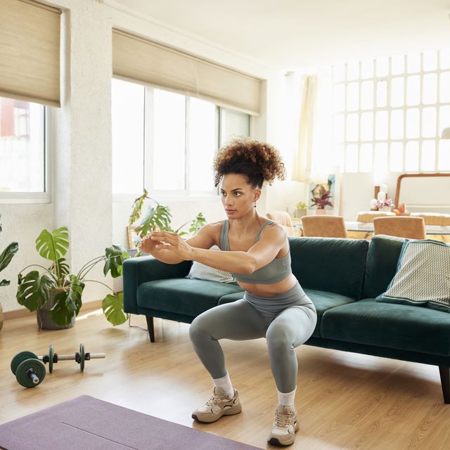 young fit woman doing squats in living room