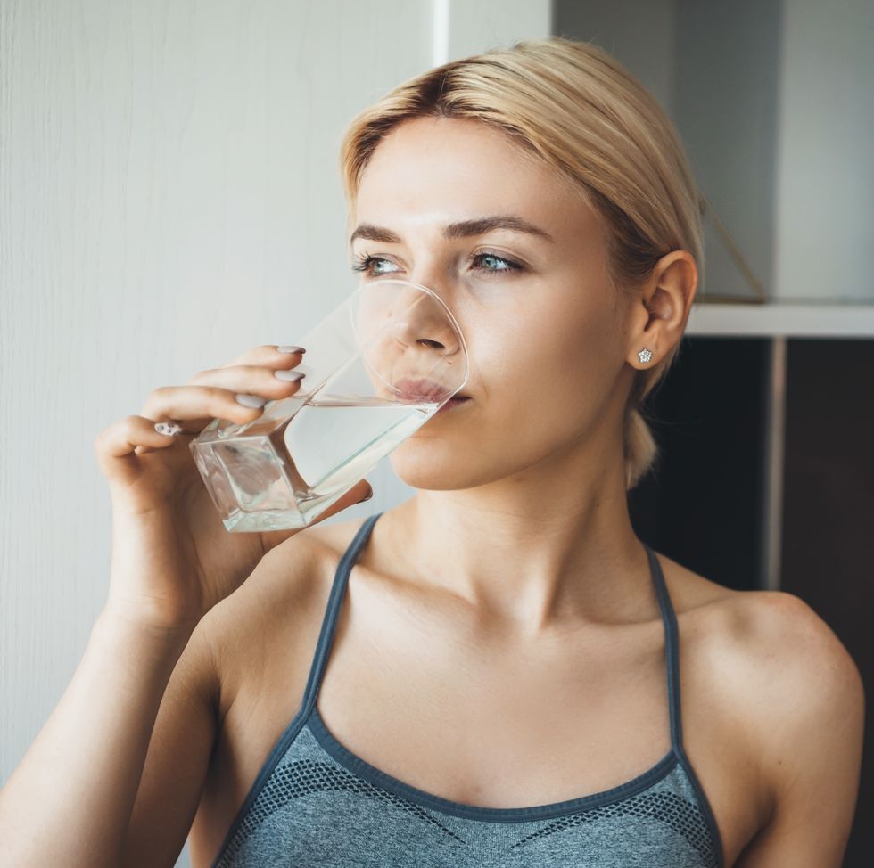 young fitness lady drinking water after yoga exercises wearing sportswear at home in the kitchen