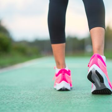 young fitness sport woman running on the road in the morning, runner feet running on road closeup on shoe. athletes legs walking on street for summer marathon.