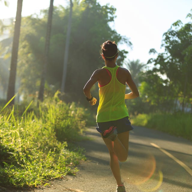 young fitness woman running at morning tropical forest trail