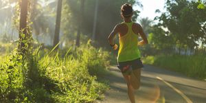 young fitness woman running at morning tropical forest trail