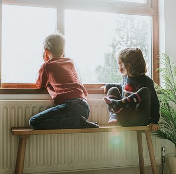 young girl and boy sit on a bench by a sunny window and gaze out