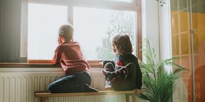 young girl and boy sit on a bench by a sunny window and gaze out