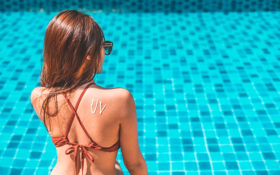 Young girl has uv word on her back made of sun cream at the beach. Sun protection factor concept. Sunscreen, Sun tan lotion sun drawing on woman back. Girl in bikini sitting on swimming pool in sunlight.