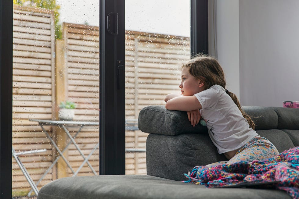 una niña mira por la ventana en un día de lluvia