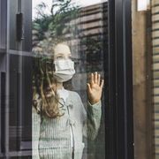 young girl looking through window with mask