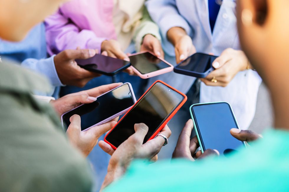 young group of people standing in circle using mobile phones outside unrecognizable teen friends watching social media content on smartphone app technology lifestyle concept