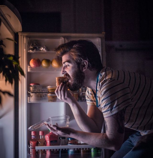 Young handsome man eating late night in front of the refrigerator