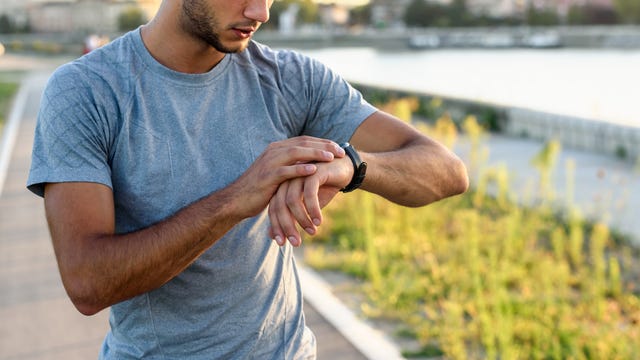 young handsome sporty jogger taking break from exercising outdoors looking on a smart fitness watch