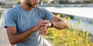 young handsome sporty jogger taking break from exercising outdoors looking on a smart fitness watch