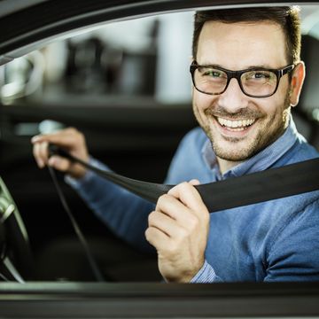 young happy man fastening his seatbelt before a trip by car