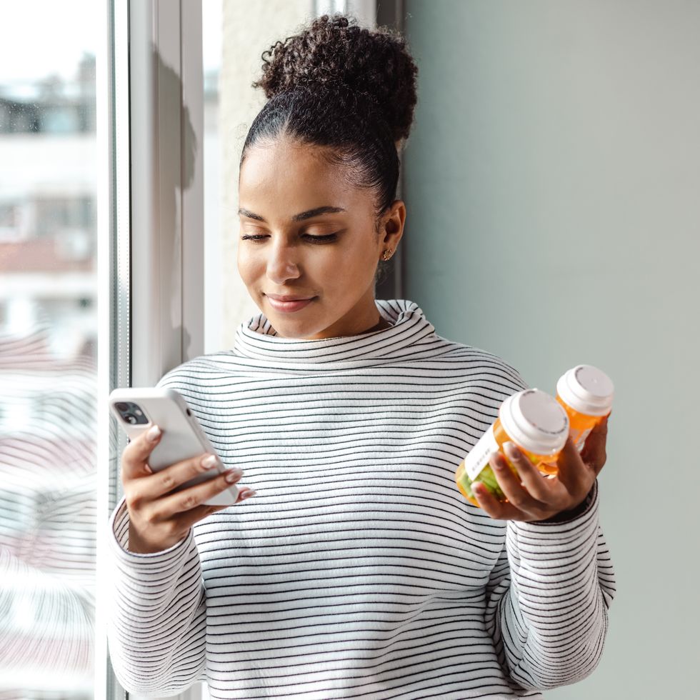 a young happy woman holding a smart phone and a pill bottle