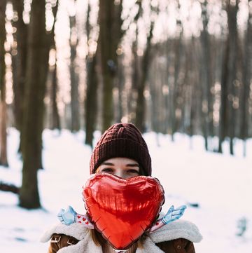 woman in snowy woods holding a red foil balloon in front of her face