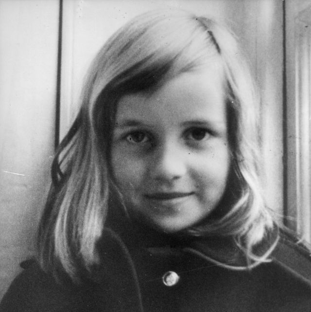 a black and white photo of lady diana spencer as a child, wearing a dark coat and smiling at the camera