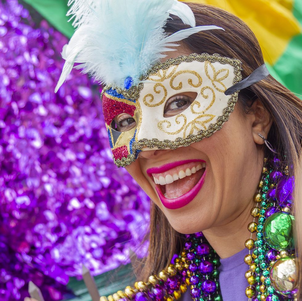 a young latin tourist female, wearing mask, costumes and necklaces celebrating mardi gras through the streets while taking a selfie with her cellphone in new orleans
