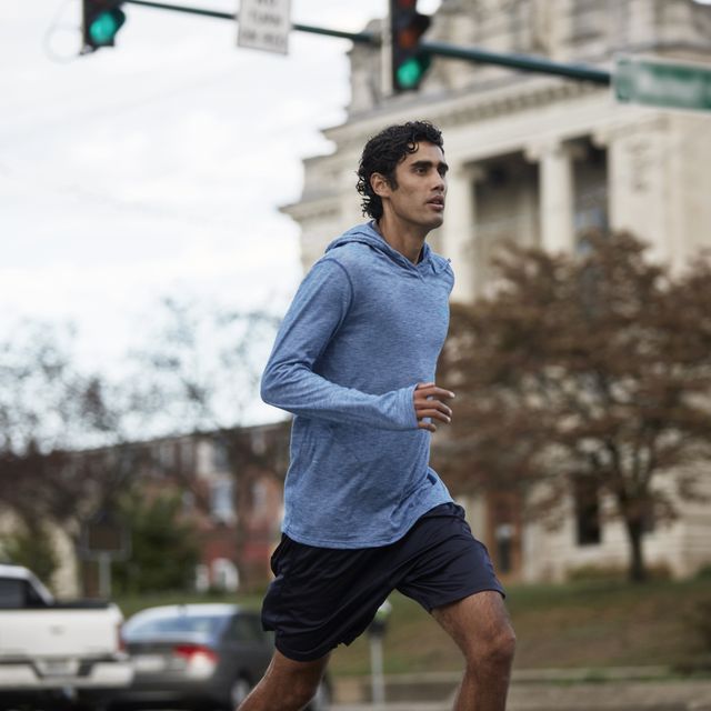 young latino man in blue sweatshirt runs by small town courthouse