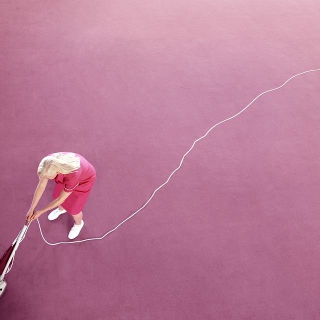 Young maid vacuuming pink carpet, elevated view