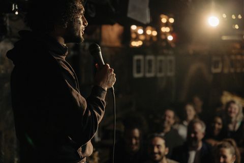 young male comedian performing stand up for audience at illuminated amateur theater