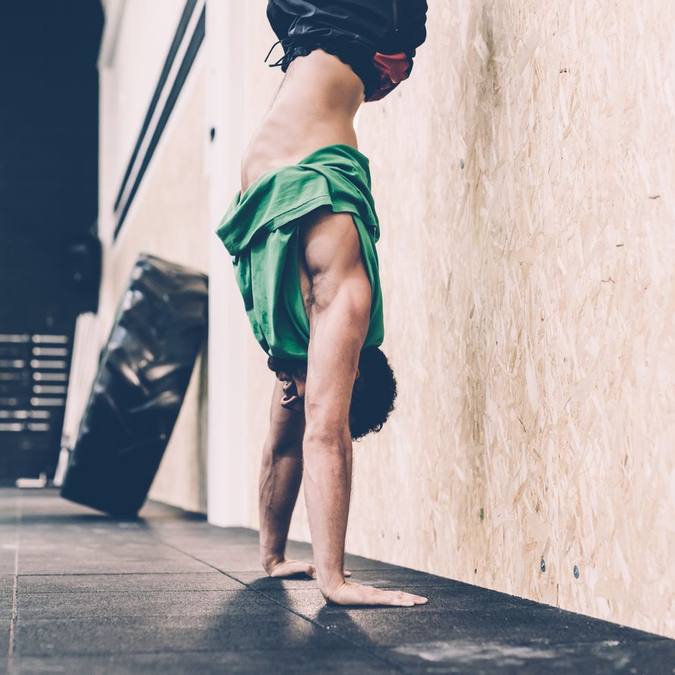 Young male cross trainer doing handstand in gym