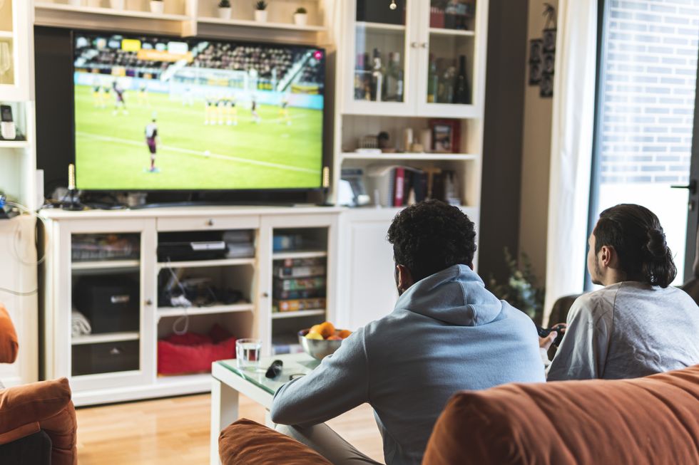 young male friends playing soccer game on television in living room at home