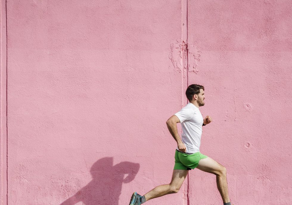 Young male runner running past pink wall