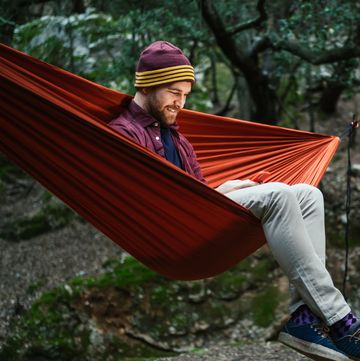 young male uses his smartphone resting on a hammock in the woods
