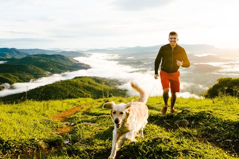 Young Man And Dog Running On Mountain Against Cloudy Sky