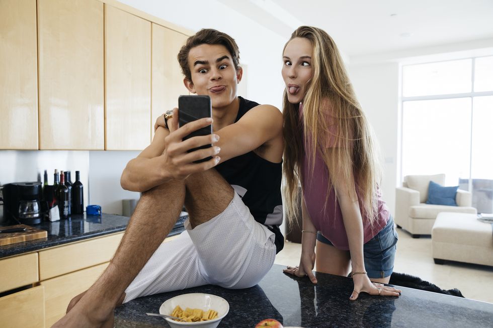 young man and sister making face while photographing selfie in kitchen
