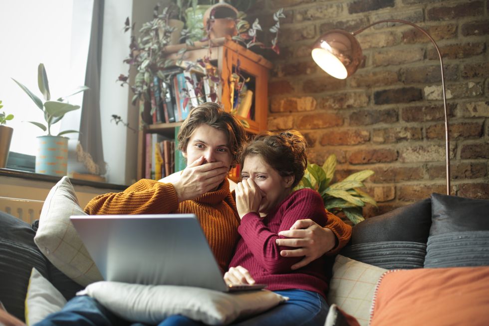 young man and woman lying on the sofa, watching an horror movie on the laptop