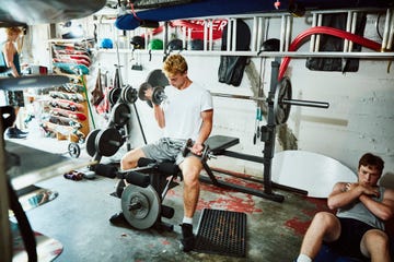 Young man doing bicep curls while working out with friends in gym in garage