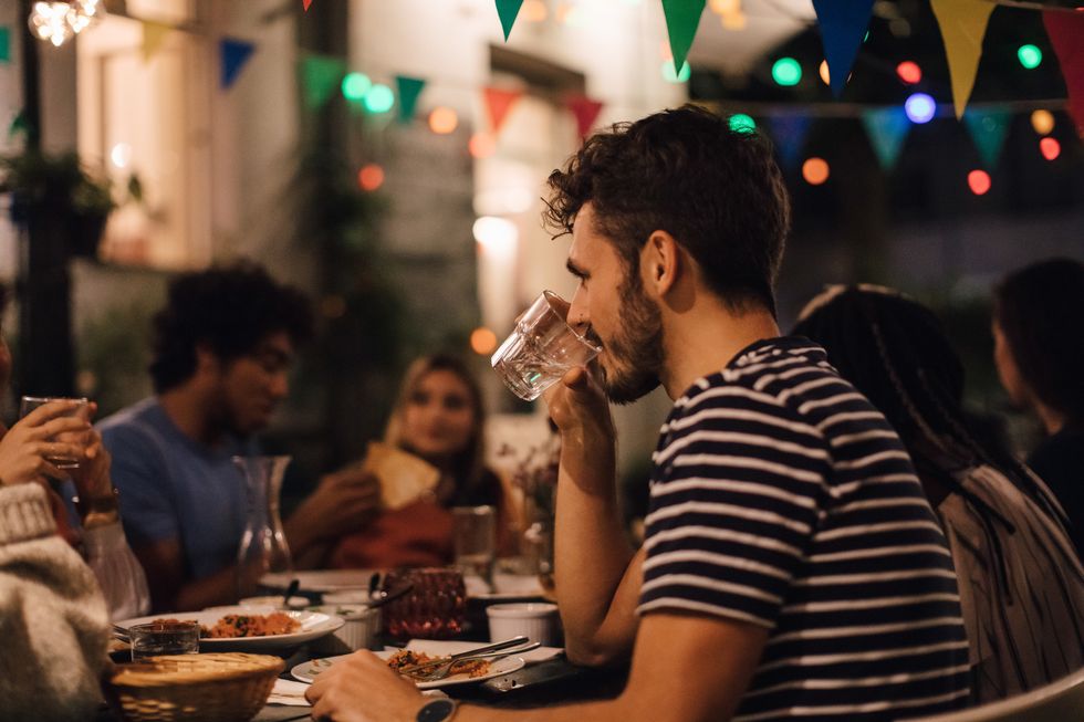 Young man drinking water while having dinner with friends during garden party