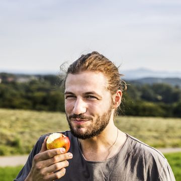 young man eating an apple in rural landscape