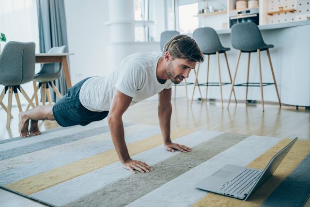 handsome young man workout at home man doing exercises while watching workout video young man using laptop while doing push ups sporty man staying in front of his laptop and watching online sport lessons man exercising and watching online fitness live streaming classes