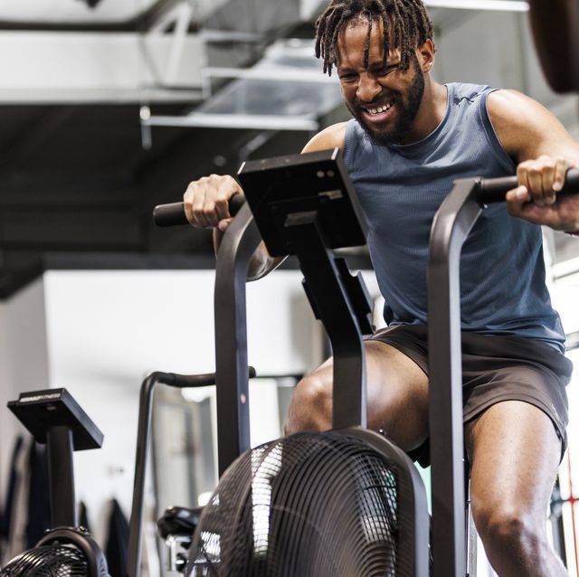 young man grimacing while exercising on bike at health club