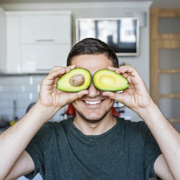 Young man having fun with avocado at the kitchen