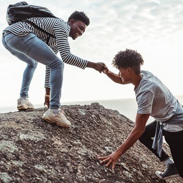 young man helping his friend to climb the rock