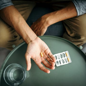 young man holding a pill in his hand in front of a table with glass of water medical treatment  drug use concept