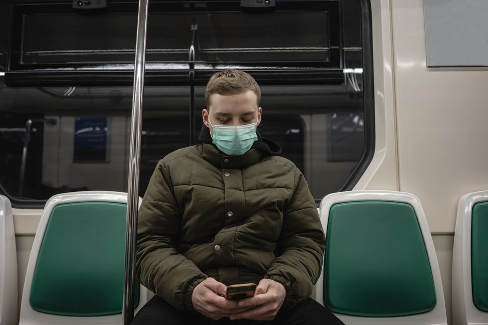 young man in commuter train, wearing face mask, using smartphone