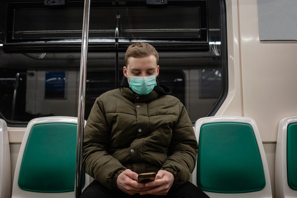 young man in commuter train, wearing face mask, using smartphone